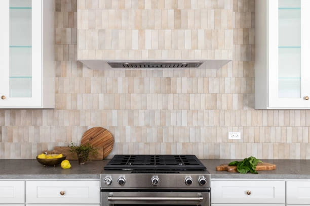 modern kitchen neutral beige. tiles backsplash, stove in the middle with few food on top of drawer, with white cabinets -backsplash tile