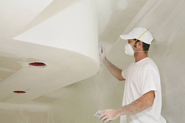 person on white with mask and helmet applying drywall on white wall -drywall contractor