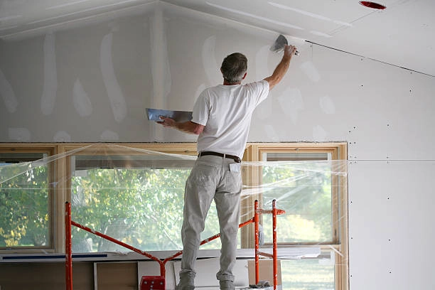 person standing applying drywall on white wall with covered window -drywall contractor