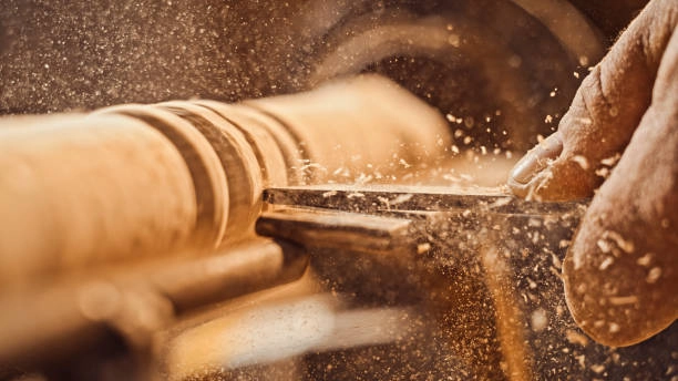 Woodworker shaping wood on a lathe, creating sawdust and shavings. -carpentry contractors