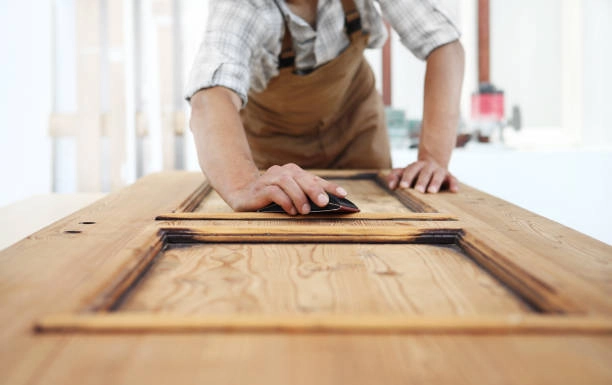 Person sanding a wooden door, smoothing the surface by hand. -carpentry contractors