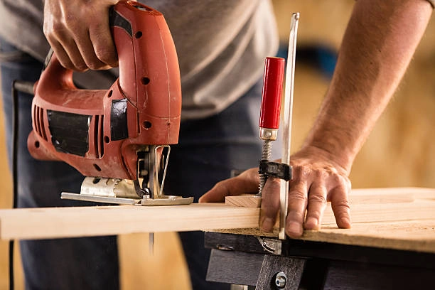 A person using a jigsaw on wood secured with a clamp. -finish carpentry tools