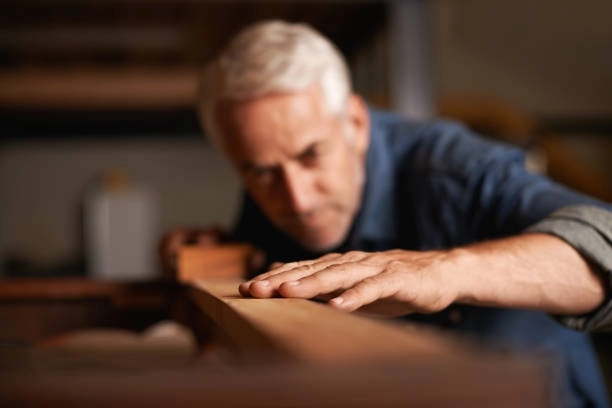 Man inspecting wood surface closely, checking for smoothness and quality. -finish trim carpentry