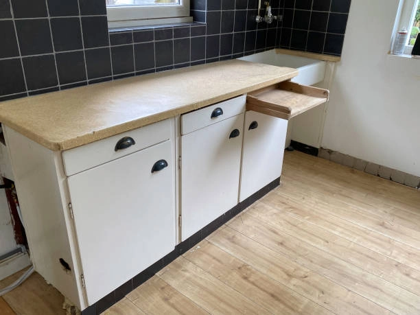 Simple kitchen counter with white cabinets, black tiles, and wood flooring. -refinishing kitchen table