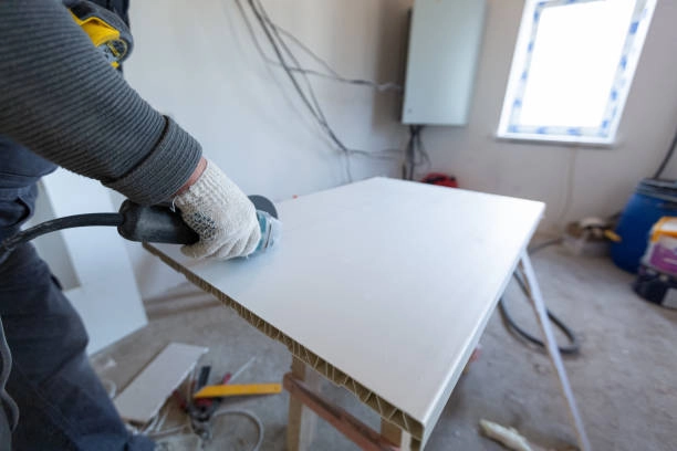 Worker sanding a panel in construction space with unfinished walls. -refinishing kitchen table