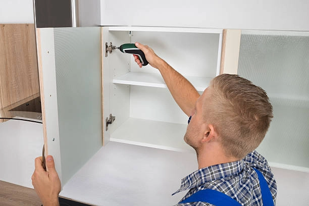 Worker installing cabinet hinges with a screwdriver in a kitchen. -refinish kitchen table