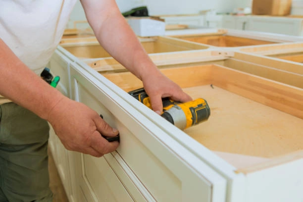 Worker installing a drawer handle on a kitchen cabinet frame. -refinish kitchen table